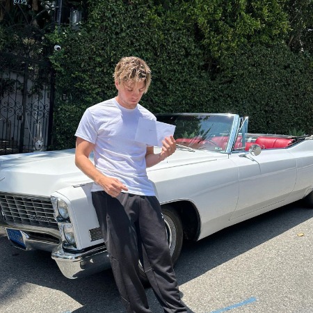 Lukas Gage posing infront of white classy car.
